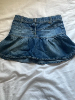 Blå volang jeanskjol - Snygg blå jeanskjol med volangkant, knappar och fickor både fram och bak. Kjolen är perfekt till sommaren och säljs på grund av att den är för liten❤️