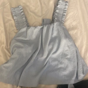 Ljusblå linnetopp med volang från H&M - Supersöt ljusblå linnetopp från H&M med breda volangprydda axelband och knyt i ryggen.