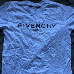 Vit Givenchy t-shirt med tryck - Säljer en vit t-shirt från Givenchy med klassiskt svart logotyp-tryck på bröstet. T-shirten har rund halsringning och korta ärmar, perfekt för en clean och stilren look.