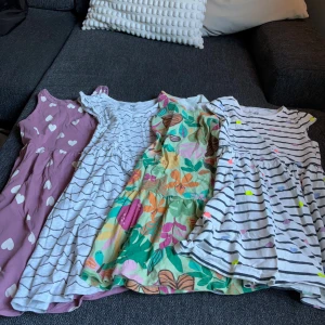 Fyra färgglada sommarklänningar H&M - Fyra söta korta klänningar från H&M i olika mönster: en lila med vita hjärtan, en vit med svarta vågor, en färgglad blommig och en vit med svarta ränder och färgprickar. Alla är ärmlösa eller med kort ärm och i mjuk bomull. Perfekta för varma dagar!