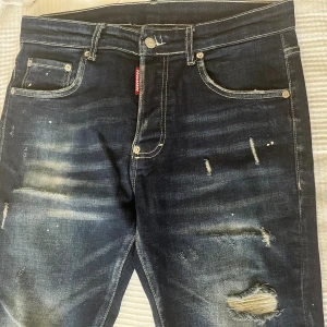 Dsquared2 jeans  - SNABB AFFÄR. Skit snygga!!!! Och billigt.. Mörkblå jeans från Dsquared2 med slitningar och hål på benen, samt coola detaljer som färgstänk och tydliga kontrastsömmar. Klassisk femficksmodell med röd Dsquared2-tag och stor röd patch bak i midjan. Jeansen har en smal passform och är tillverkade i jeansmaterial.