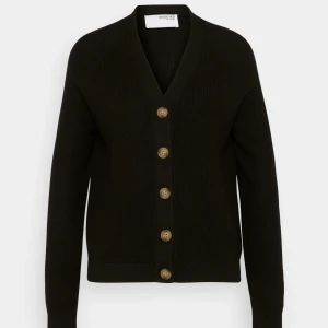 Svart kofta från Selected Femme - Svart kofta från Selected Femme med snygg v-ringning och stora bruna knappar framtill. Koftan är ribbstickad och har långa ärmar, perfekt att slänga på över en t-shirt. Materialet är mjukt och känns skönt mot huden. Använd fåtal gånger.