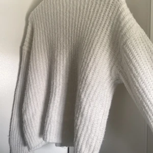 Vit stickad tröja med grov struktur - Mysig vit stickad tröja med grov ribbad struktur och rund hals. Tröjan är tillverkad av en blandning av återvunnen polyester, polyamid, ull och elastan vilket gör den både mjuk och stretchig. Perfekt för lager-på-lager under kyliga dagar.