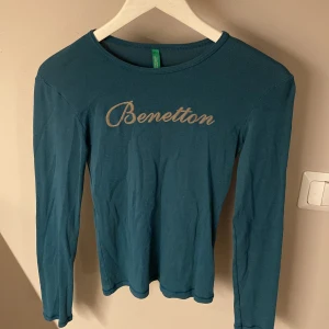 Blå långärmad tröja från Benetton XS - Snygg blå långärmad tröja från Benetton med broderad logga framtill, storlek XS. Tröjan har en klassisk rund halsringning och är gjord i mjuk bomull, perfekt för en chill och stilren look.