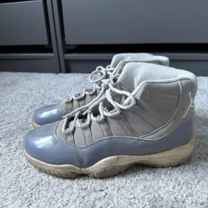 Grå Air Jordan 11 - Snygga Nike Air Jordan 11 i färgen Cool Grey och storlek 42, vit sula och grått patentläder runt om. Skorna har klassisk snörning, vit Jumpman-logga på hälen och en blandning av syntet och skinnmaterial. Perfekta för dig som gillar streetwear och ikoniska sneakers.