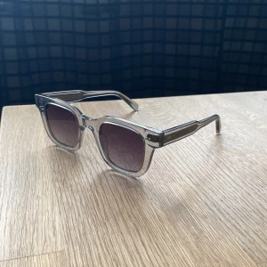 Chimi glasögon  - Snygga solglasögon med transparent, fyrkantig båge och mörka glas. Riktigt clean look med breda skalmar och modern vibe. Perfekta för dig som vill sticka ut med en stilren accessoar i sommar eller när som!