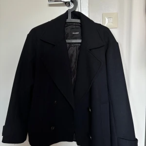 Mörkblå kappa från Pull&Bear - Stilren mörkblå kappa från Pull&Bear med breda slag, dubbelknäppning och knappar vid ärmslut. Kappan har en klassisk, rak passform och är fodrad för extra komfort. Perfekt för dig som vill ha en tidlös look med lite edge.