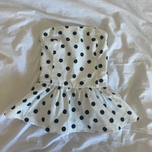 Prickig bandeau topp från Bik Bok - Supersöt vit bandeau topp från Bik Bok med svarta prickar och volang nertill. Toppen är axelbandslös och har smockad rygg för extra komfort. Prislapp kvar, kontakta för mer info💗