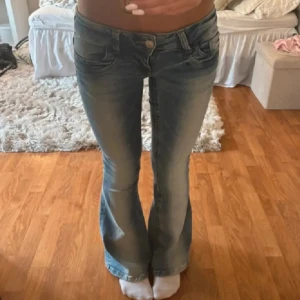 Blå bootcut jeans med låg midja - Säljer ett par snygga blå jeans med bootcut-modell och låg midja. Jeansen har klassisk femficksdesign, ljus tvätt och lätt slitna detaljer framtill. Perfekta för dig som gillar en retro vibe och vill ha ett par jeans som sitter tajt upptill och släpper vid benen.
