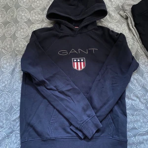 Mörkblå hoodie från Gant - Mörkblå hoodie från Gant i storlek 158/164 vilket motsvarar ungefär XS. Tröjan är knappt använd och därmed i ett bra skick. Nypris 1499kr. Mitt pris: 249
