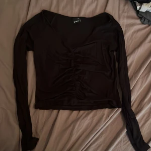 Svart v-ringad topp  - Snygg svart långärmad topp från Gina Tricot med v-ringning och rynkade detaljer framtill. Tunn och stretchig, perfekt att styla med jeans eller kjol. Enkel men trendig design som passar till många olika looks.