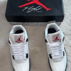 Jordan 4 - Nike Air Jordan 4 Retro i vitt, svart och grått med röda detaljer. Skorna har klassisk meshpanel, snörning och specklad grå sula. Ikonisk Jumpman-logga på plösen och Nike Air-märke under sulan. Perfekt för dig som vill sticka ut med en tidlös sneaker.