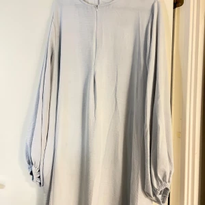 Ljusblå långklänning med ballongärmar - Enkel och stilren ljusblå långklänning med rund halsringning och långa ballongärmar med resår vid handlederna. Klänningen har en rak passform och är tillverkad i ett mjukt, lätt tyg som faller snyggt.