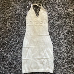 Vit stickad kortklänning H&M Divided XS - Supersöt vit stickad kortklänning från H&M Divided i storlek XS. Klänningen har halterneck med knyt i nacken, v-ringning och fina håldetaljer upptill. Den är figurnära och passar perfekt för en trendig och fräsch look.
