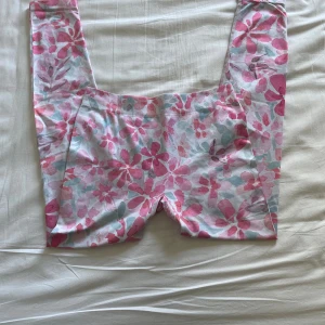 Blommiga tränings byxor - Snygga leggings med blommigt mönster i rosa, ljusblått och vitt. De har en tight passform och är perfekta för dig som gillar färg och mönster. Mjukt och stretchigt material som sitter skönt när du tränar.