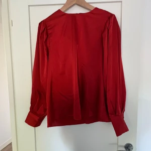 Röd blus - Säljer denna superfina röda blusen. Öppen i ryggen där man knyter en rosett. Endast använd en gång. Superfin nu till hösten!!