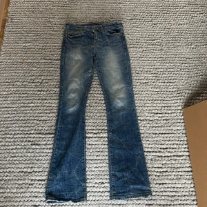 Super coola blåa low waist bootcut jeans - (Kan sänka pris)Säljer ett par blå jeans med bootcut low waist passform och snygga slitningar på knän och lår. Jeansen har klassisk femficksdesign och är tillverkade i jeansmaterial. Perfekta för dig som gillar en avslappnad och trendig look.