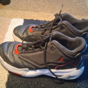 Air Jordan max aura skor - Snygga svarta Jordan sneakers med röda detaljer och vit sula. Skorna har snörning, rund tå och är tillverkade i en mix av skinn och textil. Perfekta för dig som gillar sportig stil och vill sticka ut med klassiska färgkombinationer.