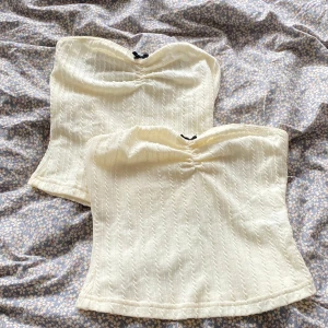 Vita ribbade tubtoppar med rosett - Två söta vita tubtoppar med ribbad struktur och liten svart rosett framtill. Topparna har bandeau-modell och lätt rynkning vid bysten för en snygg passform. Perfekta att styla med jeans eller kjol för en fräsch look. 1 för 50kr eller två för 60kr 🤗
