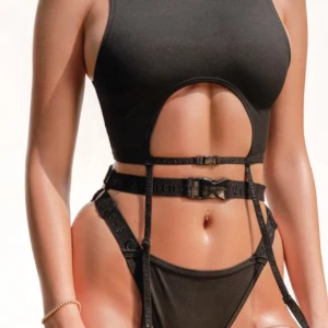 Svart gartiertopp med spännen - Svart topp med cut-out framtill och justerbara strumpebandshållare med spännen runt midjan. Snygg till träning/dans och även som bikini. Helt ny och oanvänd. 
