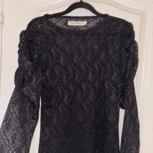Svart spetsblus med puffärm Gina Tricot - Snygg svart spetsblus från Gina Tricot med lång ärm och puffiga axlar. Blusen har ett vågigt spetsmönster och är transparent, perfekt att styla med ett linne under. Ger en cool och trendig vibe till din outfit.