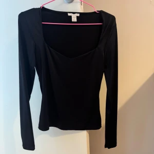 Svart långärmad topp från  - En svart långärmad topp från NA-KD med snygg v-ringad halsringning och figurnära passform. Tillverkad i mjukt och stretchigt material som känns skönt mot huden. Perfekt att styla med jeans eller kjol för en clean look.