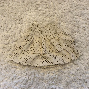 Prickig volangkjol från Zara - Supersöt kort volangkjol från Zara i beige med svarta prickar. Kjolen har inbyggda skjorts vilket är jätteskönt om man vill leka runt utan att oroa sig för att kjolen ska åka upp. Jag säljer denna kjolen för 200kr + frakt som kunden betalar, pris kan diskuteras.
