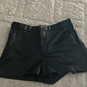 Svarta skinnshorts från Zara - Snygga svarta shorts i skinnimitation från Zara. De har bälteshällor, dragkedja och hyska fram samt klassisk passform med lite vidare ben. Perfekta för att lyfta vilken outfit som helst. Dom är rätt så små i storleken 