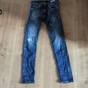 Blå Replay jeans, skinny fit, stl 29 - Säljer ett par blå Replay jeans i skinny fit med slitna detaljer och snygg tvätt. Klassisk femficksmodell med dragkedja och knapp. Jeansen har en mörkblå bas med ljusare partier och är tillverkade i stretchig denim för skön passform.