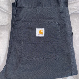 Carhartt Wip svarta jeans  - Svarta byxor från Carhartt med klassisk fyrkantig logga på bakfickan. Raka ben och normal passform, tillverkade i slitstarkt bomullstyg. Storlek 34/32