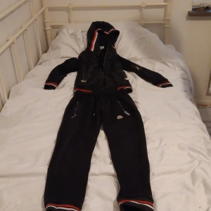 Set från Moncler strl.130 - Svarta mjukisbyxor från Moncler med vita och röda ränder vid benslut och knän. Byxorna har dragsko i midjan, dragkedjor vid fickorna och Moncler-logga på benet. Perfekta för en chill och sportig look.