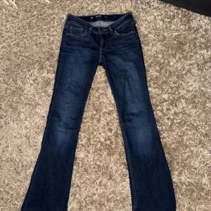 Bootcut jeans från Hollister blå W24S - Mörkblå bootcut jeans från Hollister med låg midja och klassisk stretch. Snygga detaljer på bakfickorna och klassisk femficksmodell. Perfekta om du gillar en tidlös och avslappnad look. Ordinarie pris: 500SEK.