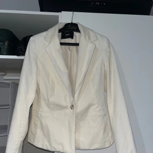 Vit manchesterkavaj från Bik Bok - Snygg vit kavaj i manchester från Bik Bok med klassisk krage och en knapp framtill. Kavajen har raka fickor och är figursydd för en stilren look. Perfekt att styla med jeans eller kjol för en trendig outfit.