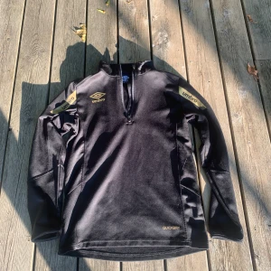 Umbro tröja storlek xs i färgen svart och guld detaljer mycket bra skick! - Umbro tröja i storlek XS. Perfekt för en avslappnad och sportig look. I Mycket bra skick! Pris: 100 kr.