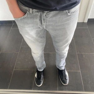 Dondup Jeans George - Säljer ett par ljusgrå skinny fit jeans från Dondup i modellen George. Jeansen har klassisk femficksdesign, smal passform och är tillverkade i mjukt denimtyg. Snyggt slitna detaljer på bakfickan och en modern look som passar till sneakers.