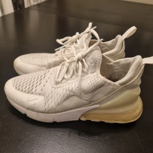 Nike Air Max 270 - Nike Air Max 270 sneakers i helvitt med mesh-överdel och tydlig Air Max-dämpning i hälen. Skorna har snörning, rund tå och en chunky sula. Snygg sportig look med diskreta loggor och dragflik bak. Perfekta för dig som gillar stilrena och bekväma sneakers.