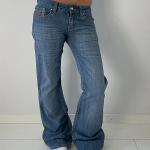 Blå bootcut jeans med broderi - Snygga blå bootcut jeans med coolt broderat mönster i brunt och beige på bakfickorna. Jeansen har låg midja, klassisk femficksdesign och är tillverkade i mjukt denim. Perfekta för dig som gillar en avslappnad och trendig look.