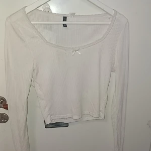 Vit ribbad långärmad topp H&M - Supersöt vit ribbad topp från H&M med lång ärm och croppad passform. Urringad hals med spetskant och liten rosett framtill ger en gullig vibe. Har några fläckar för jag krassa med cykel i den.. kan nog fixas med blekningsmedel? Eller färga den🥲