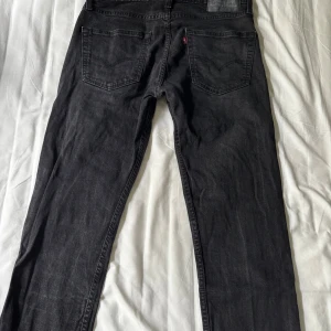 Levi's 502 svarta jeans W32 L32 - Svarta Levi's 502 jeans med klassisk femficksdesign och raka ben. Jeansen har en mörk tvätt och är tillverkade i slitstarkt bomullsjeans. Perfekta för dig som gillar en clean och tidlös look.