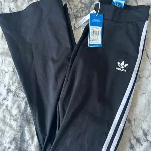 Svarta leggings från Adidas Originals - Svarta Adidas Originals leggings med vita ränder längs sidorna och klassisk logga på höften. Tight passform och midwaist. Tillverkade i mjukt och stretchigt material som sitter skönt hela dagen.