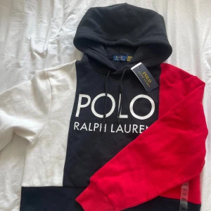Färgglad hoodie från Polo Ralph Lauren XS - Dam hoodie Säljer en hoodie från Polo Ralph Lauren i färgerna svart, vitt och rött. Tröjan har stor logga framtill, huva med snörning och är tillverkad i mjuk bomull. Perfekt för dig som gillar streetstyle och vill sticka ut med en färgstark look.