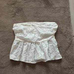 Vit broderad tubtopp med volang - Supersöt vit tubtopp med broderade blommor och volang nertill. Toppen är ärmlös och har resår upptill och baktill för en bekväm passform. Perfekt för varma dagar och ger en romantisk vibe till din outfit.  Storlek xs men passar mig som har s 