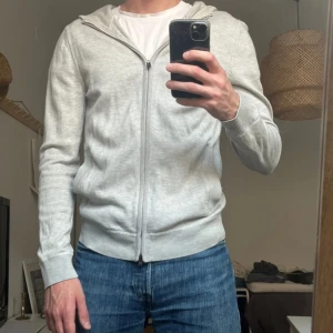 Hugo BOSS i kashmirmix - Ljusgrå hoodie från BOSS med dragkedja och huva. Tillverkad i en lyxig mix av ull, bomull och kashmir. Regular fit med ribbade muddar och fickor framtill. Perfekt för en clean och stilren look.