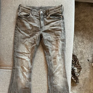 Grå bootcut jeans  - Snygga grå jeans från H&M med bootcut-modell och broderad rosett på bakfickan. Jeansen har klassisk femficksdesign, knappstängning och är tillverkade i mjukt denimtyg. Perfekta för dig som gillar en lite retro vibe och vill sticka ut med detaljer. Lite små på mig men hade passat perfekt på någon som har 32 i storlek och är 162 cm ungefär 