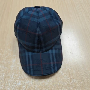 Burberry keps grå - Snygg grå keps från Burberry med klassiskt rutigt mönster i mörka toner. Kepsen har böjd skärm och är tillverkad i ett slitstarkt material som känns lyxigt. Perfekt accessoar för en stilren look.