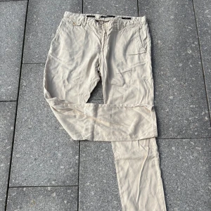 Beige slim fit chinos från Alberto - Snygga beige chinos från Alberto i slim fit-modell. Byxorna har klassiska sidfickor, bälteshällor och knäppning fram. Perfekta för en clean och stilren look, tillverkade i mjukt bomullstyg som känns skönt mot huden.
