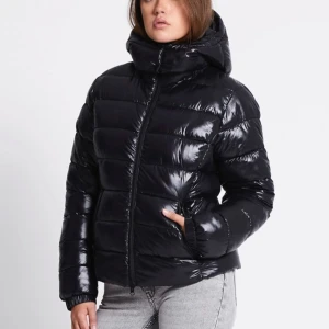 Svart glansig pufferjacka med huva - Säljer en svart pufferjacka med glansig finish och huva.Perfekt för kalla dagar. Passformen är normal.