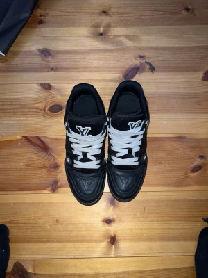 LV Trainers - Säljer ett par svarta Louis Vuitton sneakers med vita snören och tydliga LV-loggor på tungan och sidan. Skorna har en chunky sula, rund tå och är tillverkade i skinn med snygga detaljer och präglade monogram. Kommer med originalkartong och tillbehör.