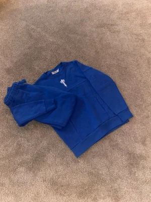 Blå Trapstar sweatshirt XS - Säljer en blå sweatshirt från Trapstar i storlek XS. Tröjan har ett stort vitt T broderat på bröstet och är gjord i mjuk bomull med ribbade muddar. Perfekt för en chill och streetwear-inspirerad look.