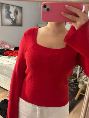 Röd stickad tröja med fyrkantig ringning - Säljer en röd stickad tröja med lång ärm och snygg fyrkantig ringning. Tröjan har en figurnära passform och är ribbstickad vilket ger en schysst struktur. Perfekt att styla med jeans eller kjol för en trendig look.